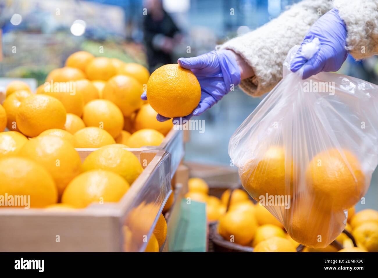 Woman hands in medical gloves chooses fresh oranges folding in a disposable plastic bag in supermarket, close up. Protective measures against coronavi Stock Photo