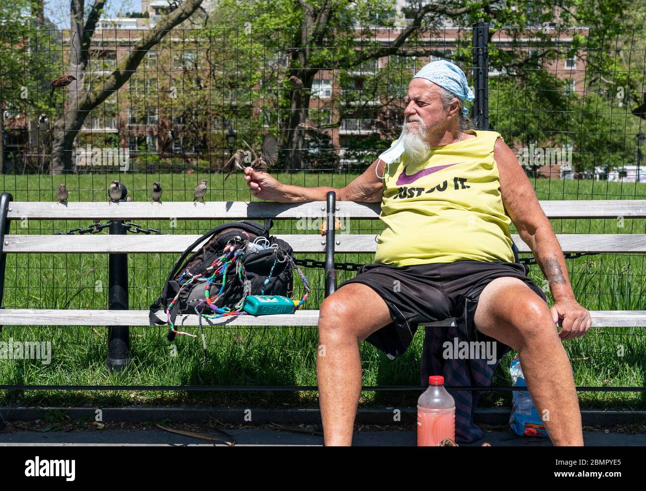 New York, NY - May 10, 2020: A man named Ronnie feed sparrows and enjoys sunny day amid COVID-19 pandemic in Washington Square Park Stock Photo
