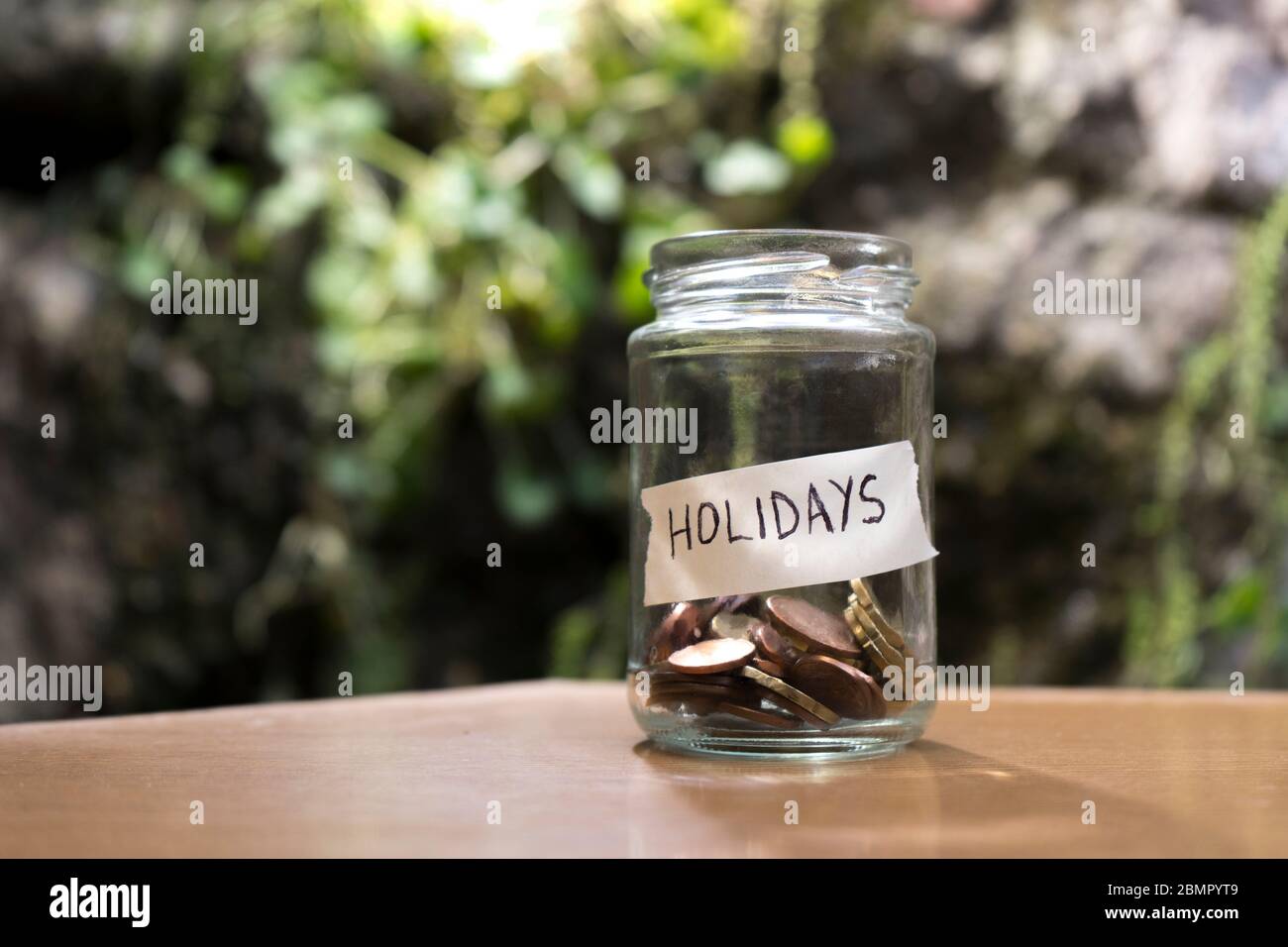 A glass jar with coins inside and a 'vacaciones' tag on a wooden. Un bote de cristal con monedas dentro, tiene una etiqueta que pone vacaciones sobre Stock Photo