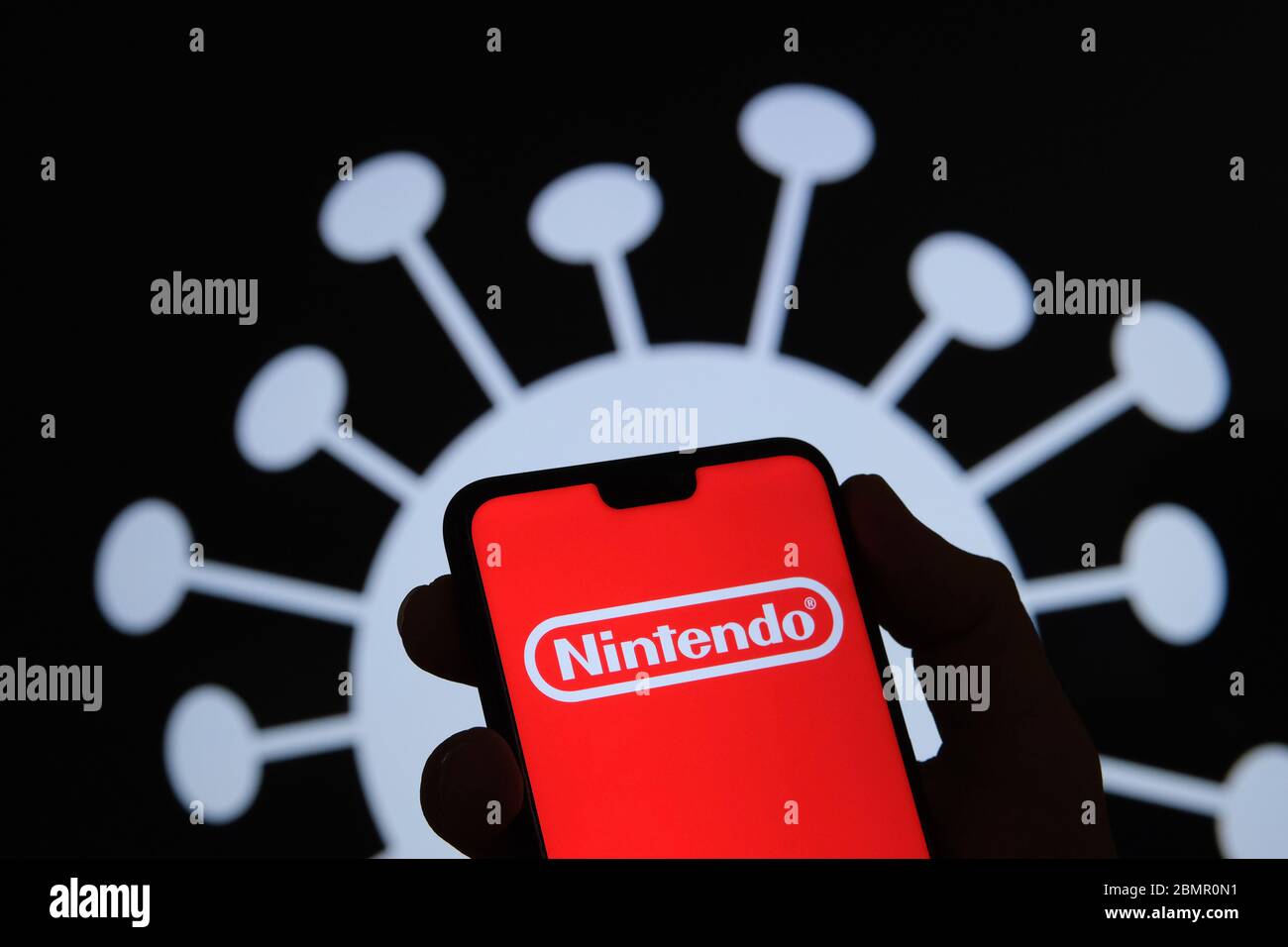 Nintendo company logo on a smartphone silhouette hold in hand. Coronavirus image on the blurred background. Real photo, not a montage. Stock Photo