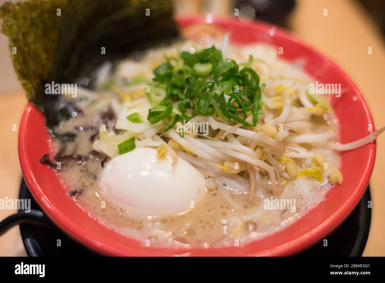 Bowl of ramen soup with fresh bean sprouts and egg garnished with dried nori seaweed sheet and green spring onions Stock Photo