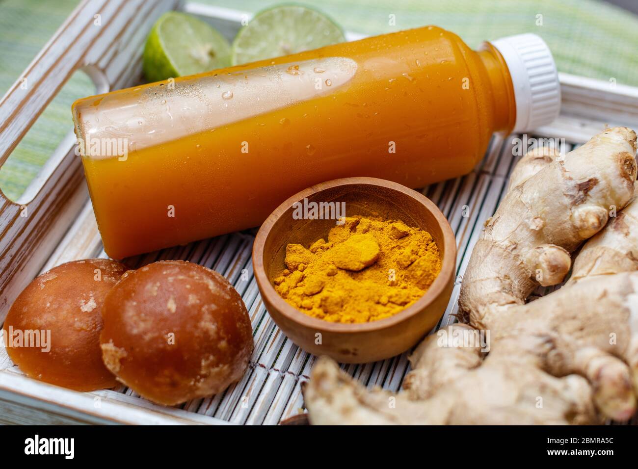 A bottle of Jamu 'Kunir Asam', traditional Indonesian herbal tonic medicine, with ingredients (ginger, turmeric, palm sugar). Bali, Indonesia. Stock Photo