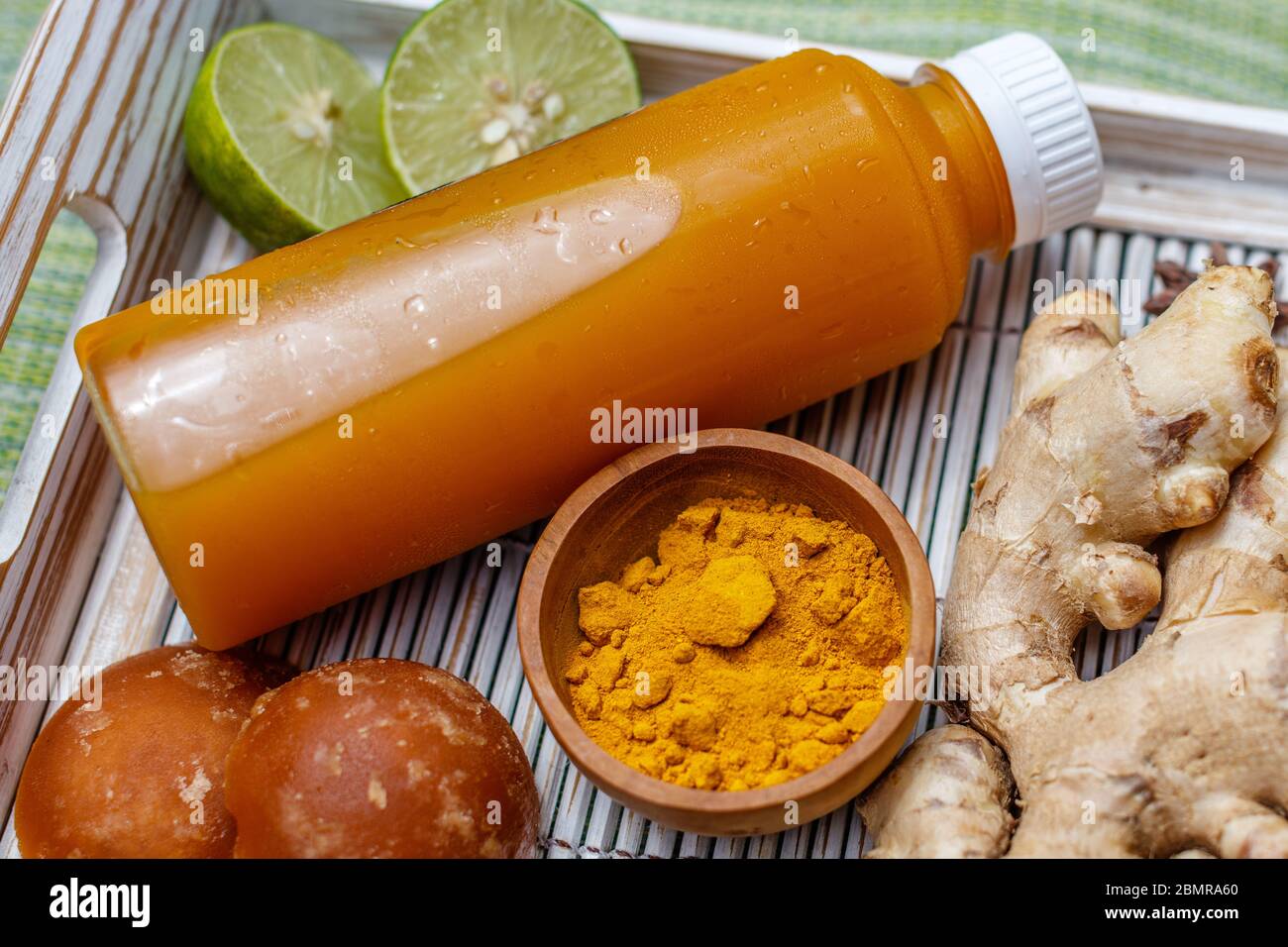 A bottle of Jamu 'Kunir Asam', traditional Indonesian herbal tonic medicine, with ingredients (ginger, turmeric, palm sugar). Bali, Indonesia. Stock Photo