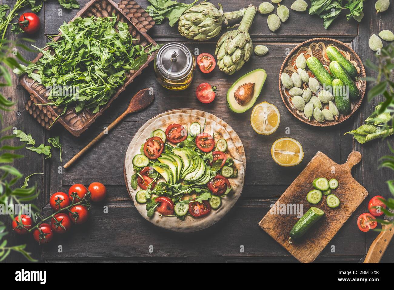 Healthy lunch making preparation. Tortilla wraps with fresh vegetables, avocado , olives oil and lemon on rustic wooden kitchen table , top view. Cook Stock Photo