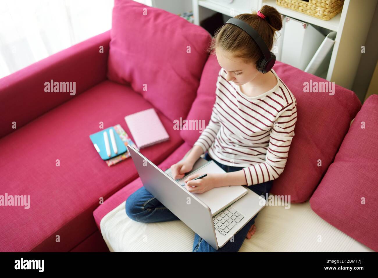 Preteen schoolgirl doing her homework with laptop computer at home ...