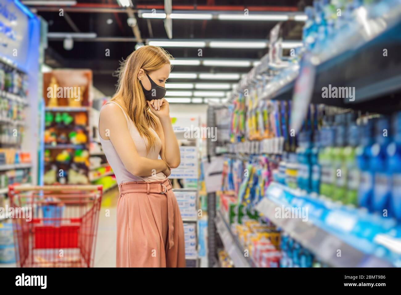 Alarmed female wears medical mask against coronavirus while purchase of household chemicals in supermarket or store- health, safety and pandemic Stock Photo