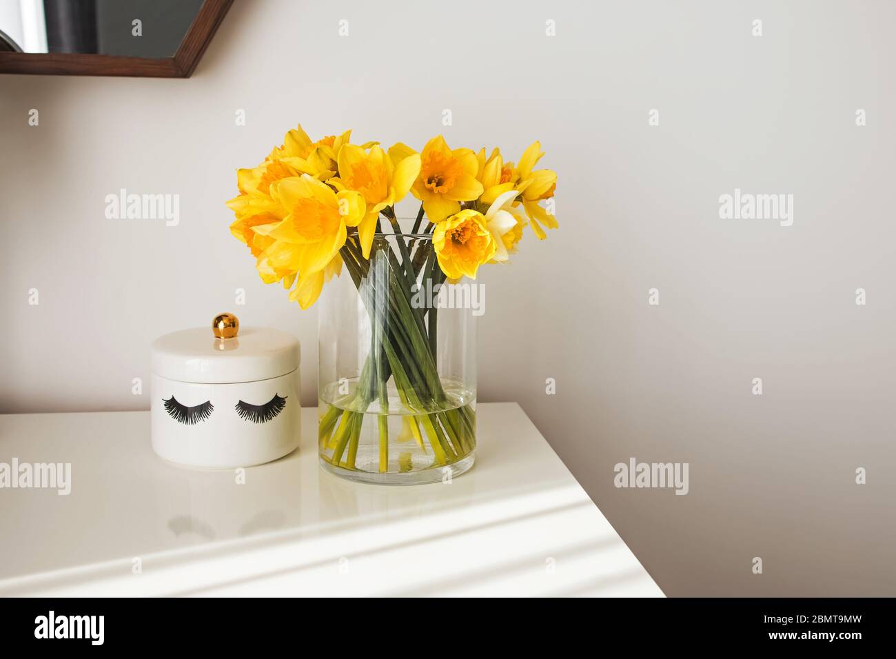 Modern minimalist white room interior with yellow flowers satnding on the table in natural sunlight from the window Stock Photo