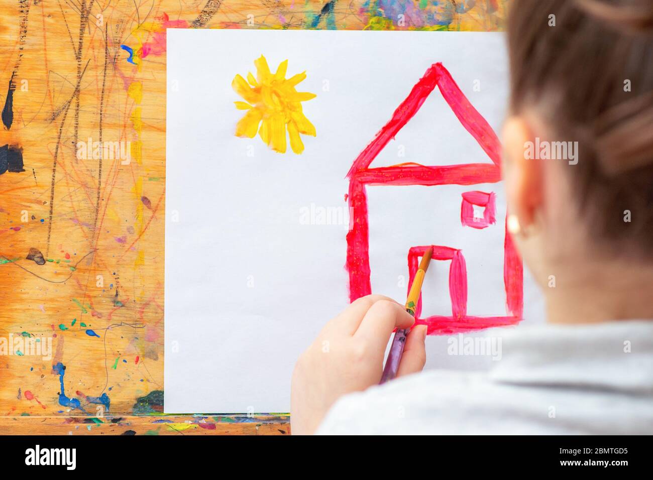 Child is drawing house with watercolors on the easel. Stock Photo