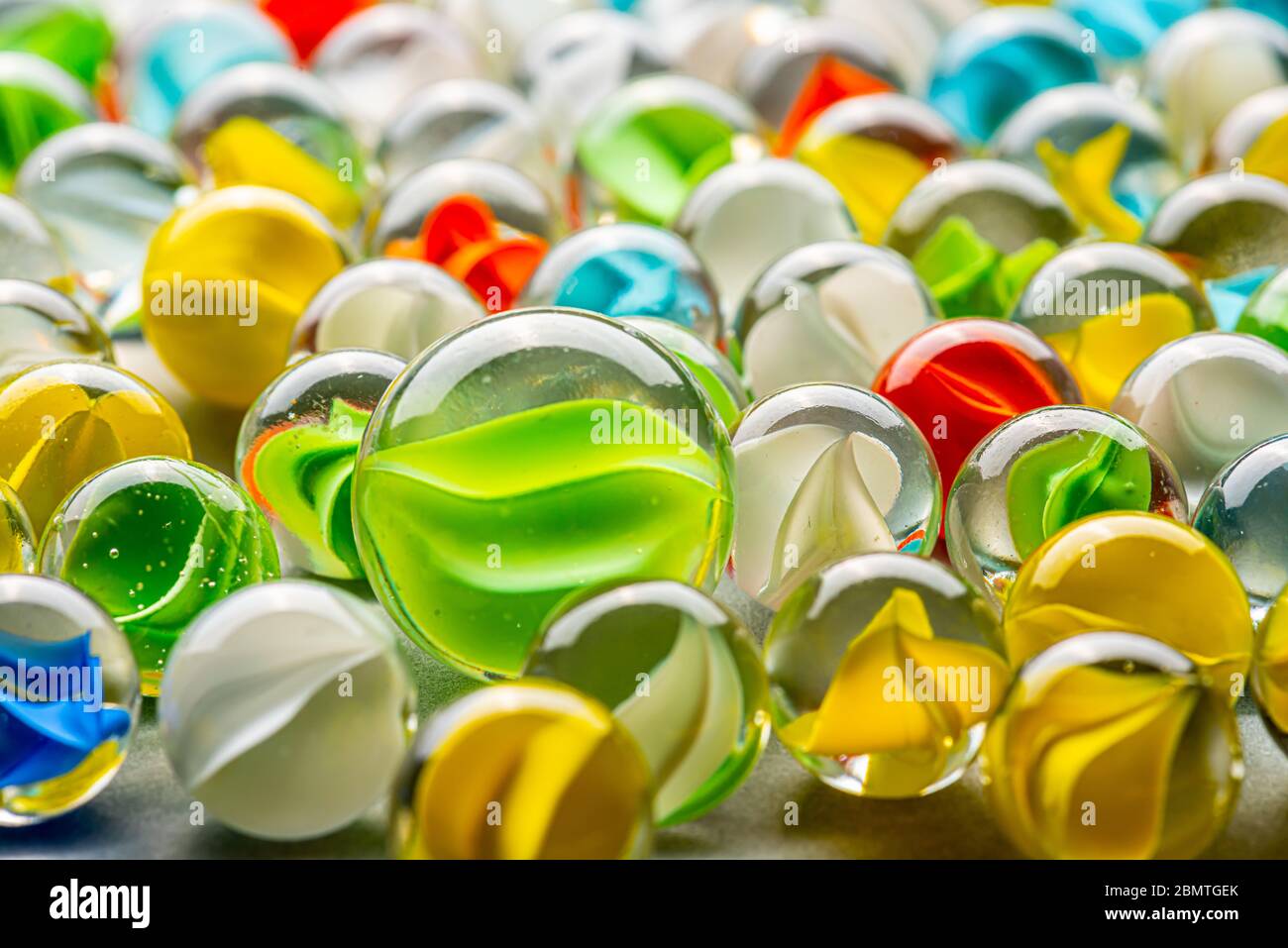 A big green glass marble between yellow, green, blue and red marbles on a  table Stock Photo - Alamy