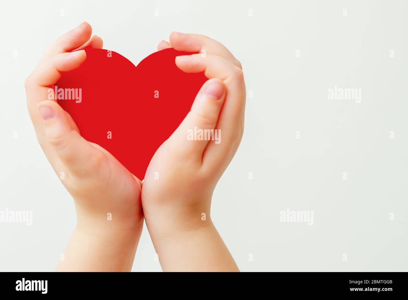 Closeup of child's hands holding paper red heart on white background. Concept of love. Stock Photo