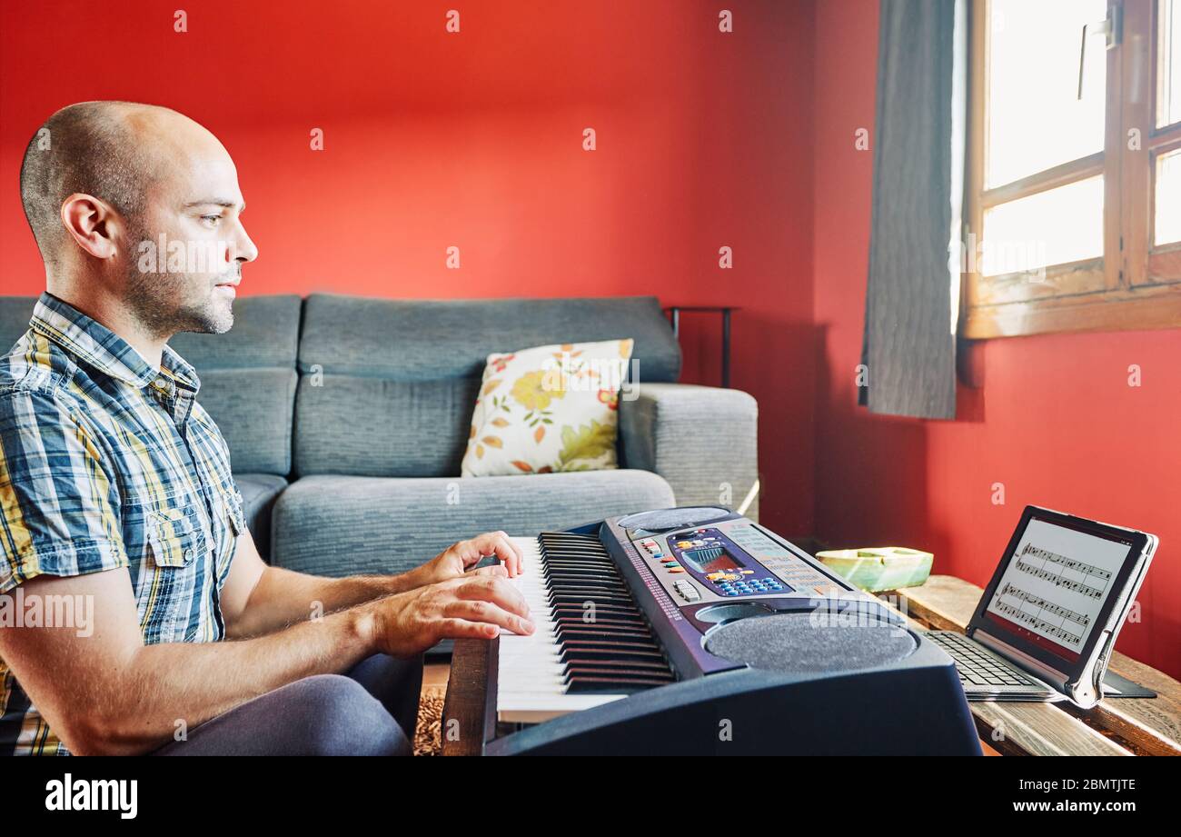 Man playing piano while taking online lessons at home. Stock Photo