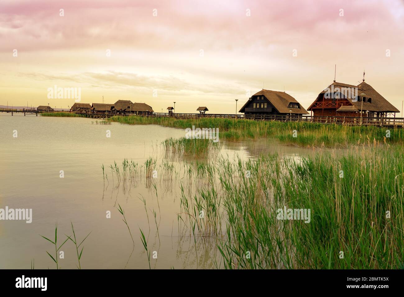 peaceful nature at the Lake Fertő in Hungary with wooden pier bungalows cabins on the lake and straw in the water at sunset Stock Photo