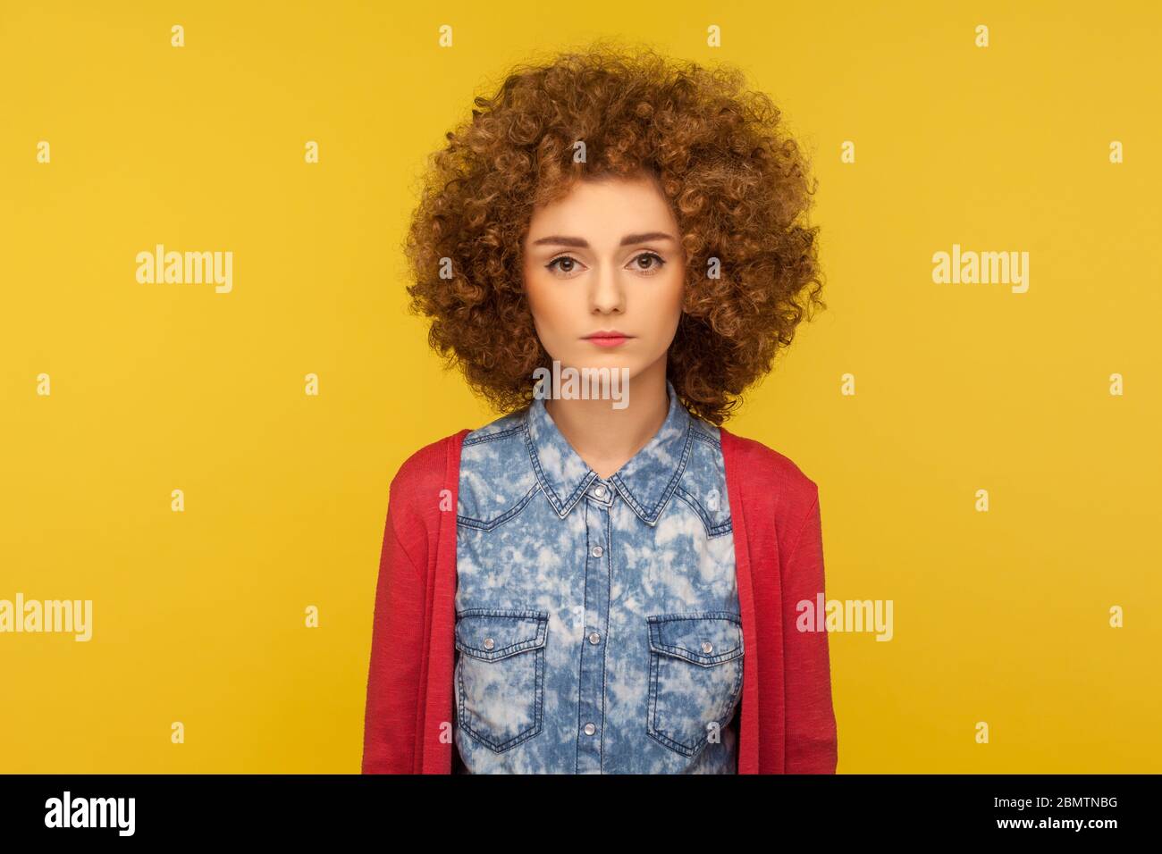Portrait of woman with curly hair in casual style jeans shirt looking at camera with serious unhappy expression, model unsmiling and looking depressed Stock Photo