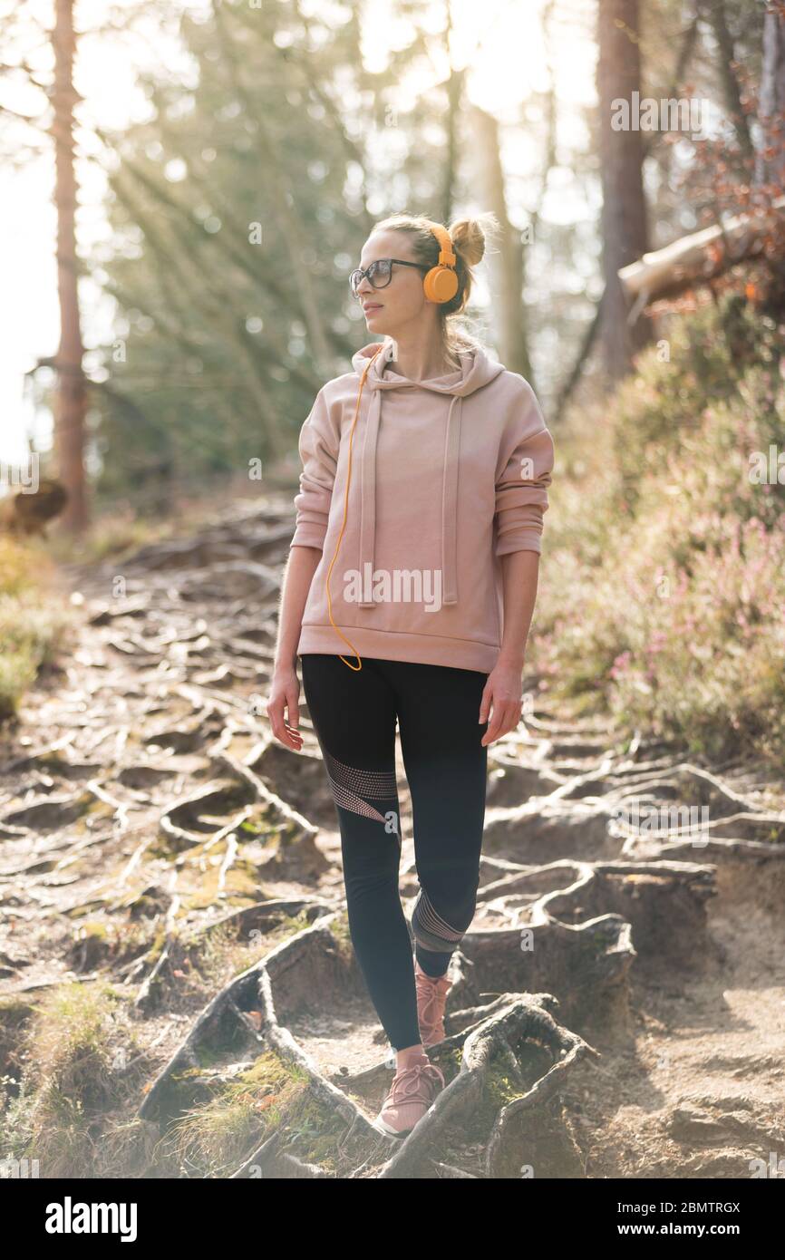 Active sporty woman listening to the music while hiking in autumn fall forest. Female jogger training outdoor. Healthy lifestyle image of young Stock Photo