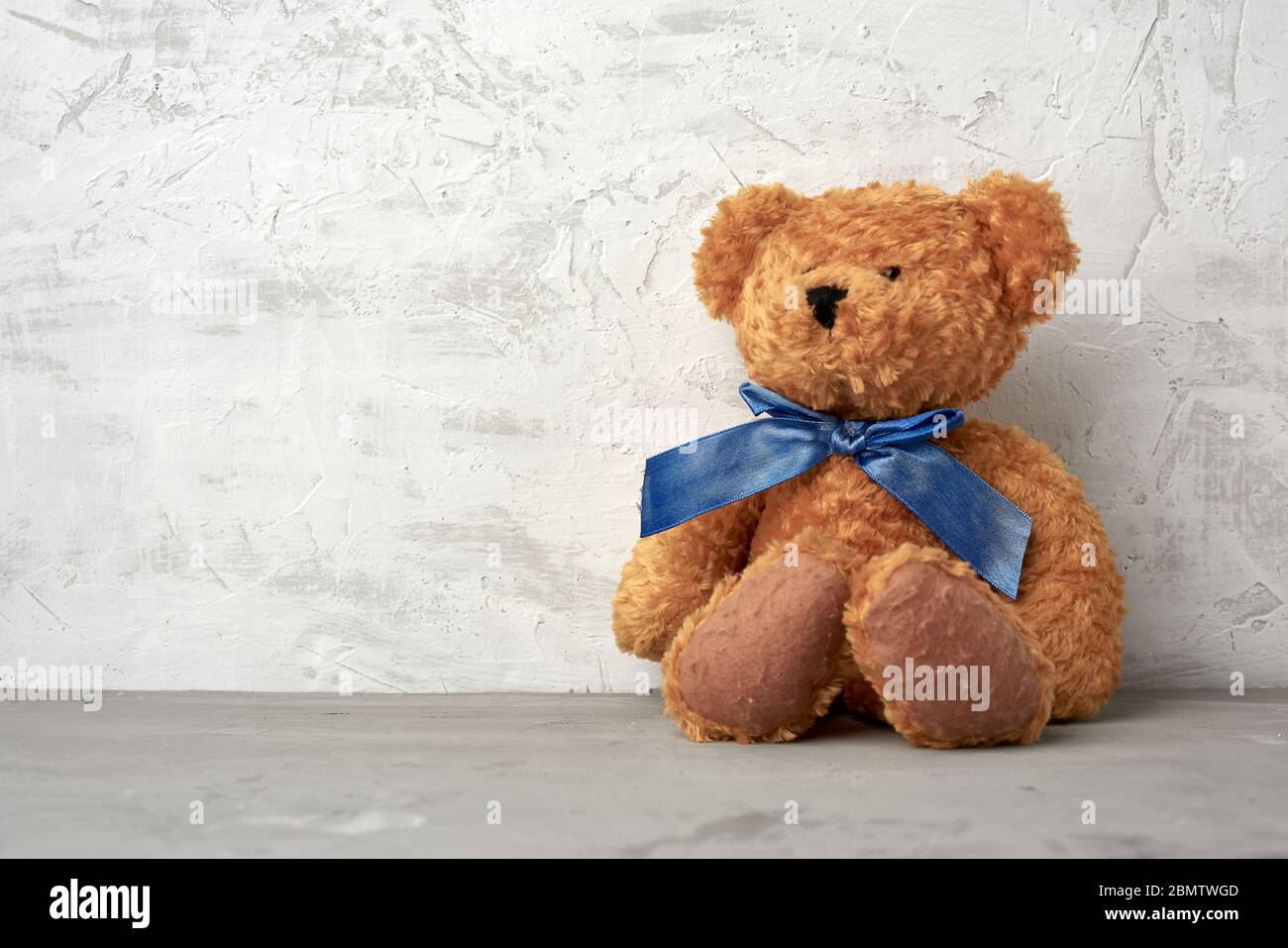 brown teddy bear with a blue bow sits on a white background, place for ...