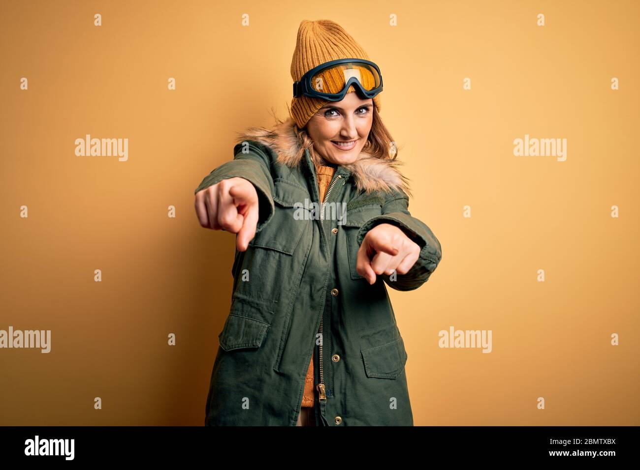 Middle age beautiful blonde skier woman wearing snow sportwear and ski goggles pointing to you and the camera with fingers, smiling positive and cheer Stock Photo