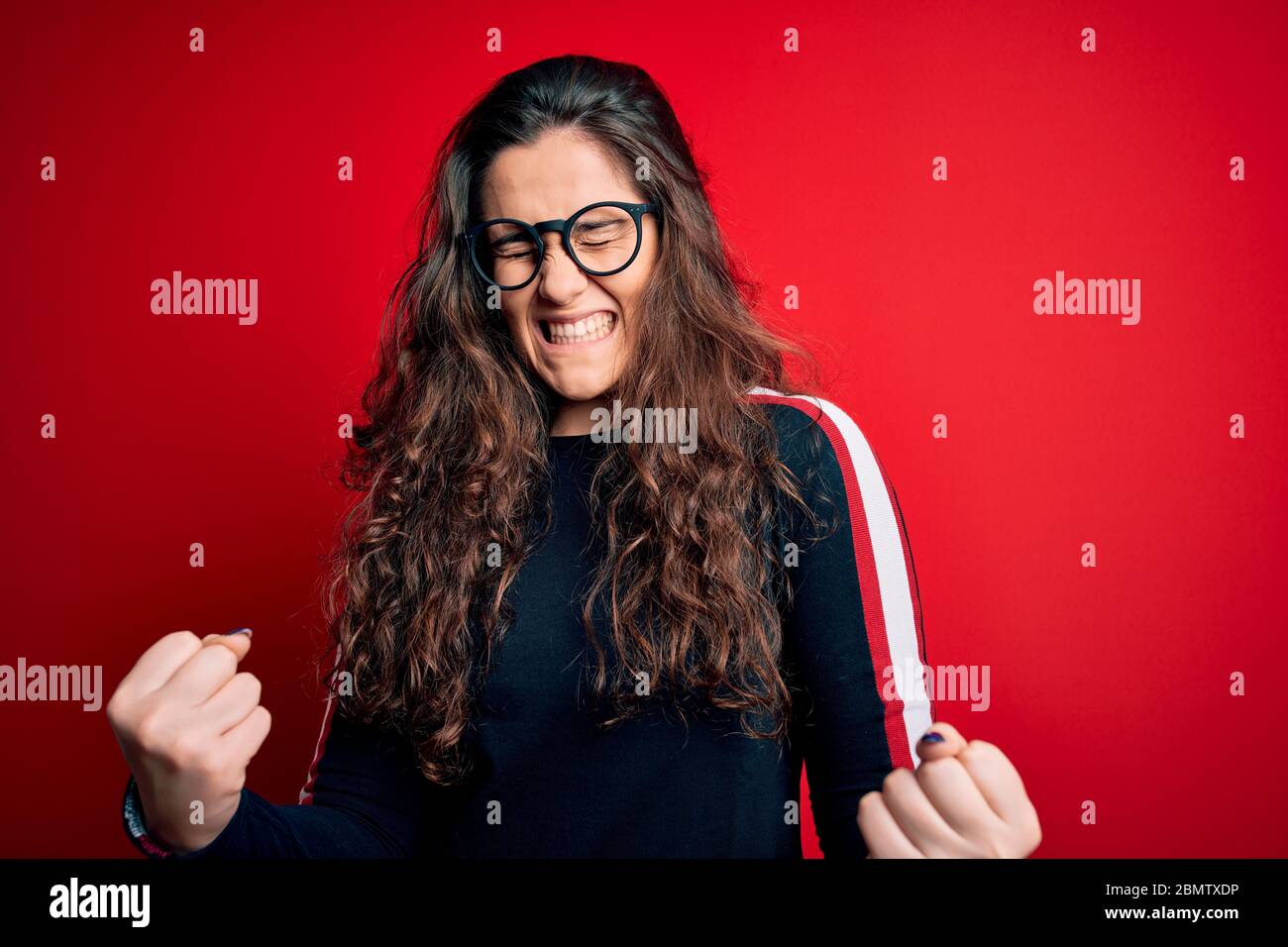 Young beautiful woman with curly hair wearing sweater and glasses over ...