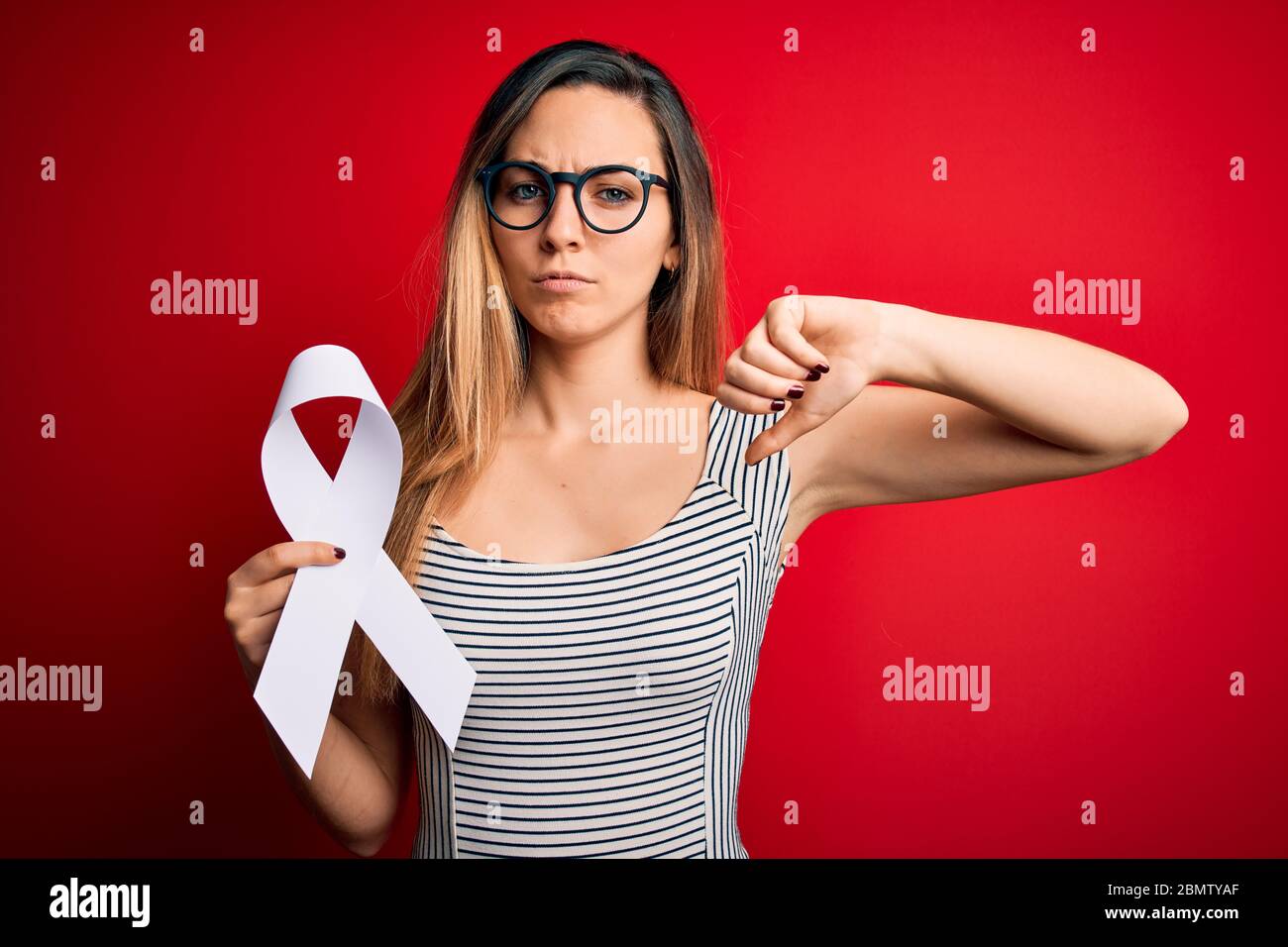 Young beautiful blonde woman with blue eyes holding white ribbon over ...