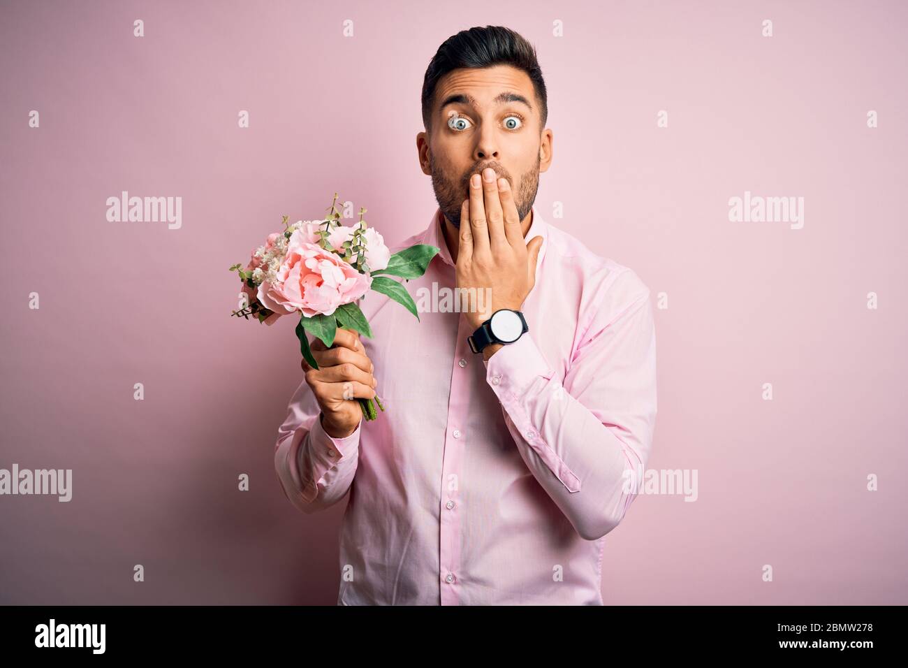 Young romatic man holding bouquet of spring flowers over pink isolatd ...