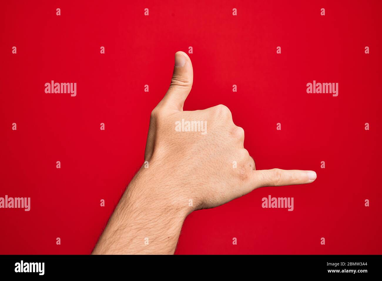 Hand of caucasian young man showing fingers over isolated red background gesturing Hawaiian shaka greeting gesture, telephone and communication symbol Stock Photo
