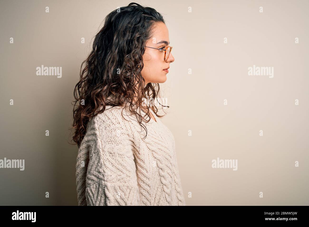 Beautiful woman with curly hair wearing casual sweater and glasses over ...