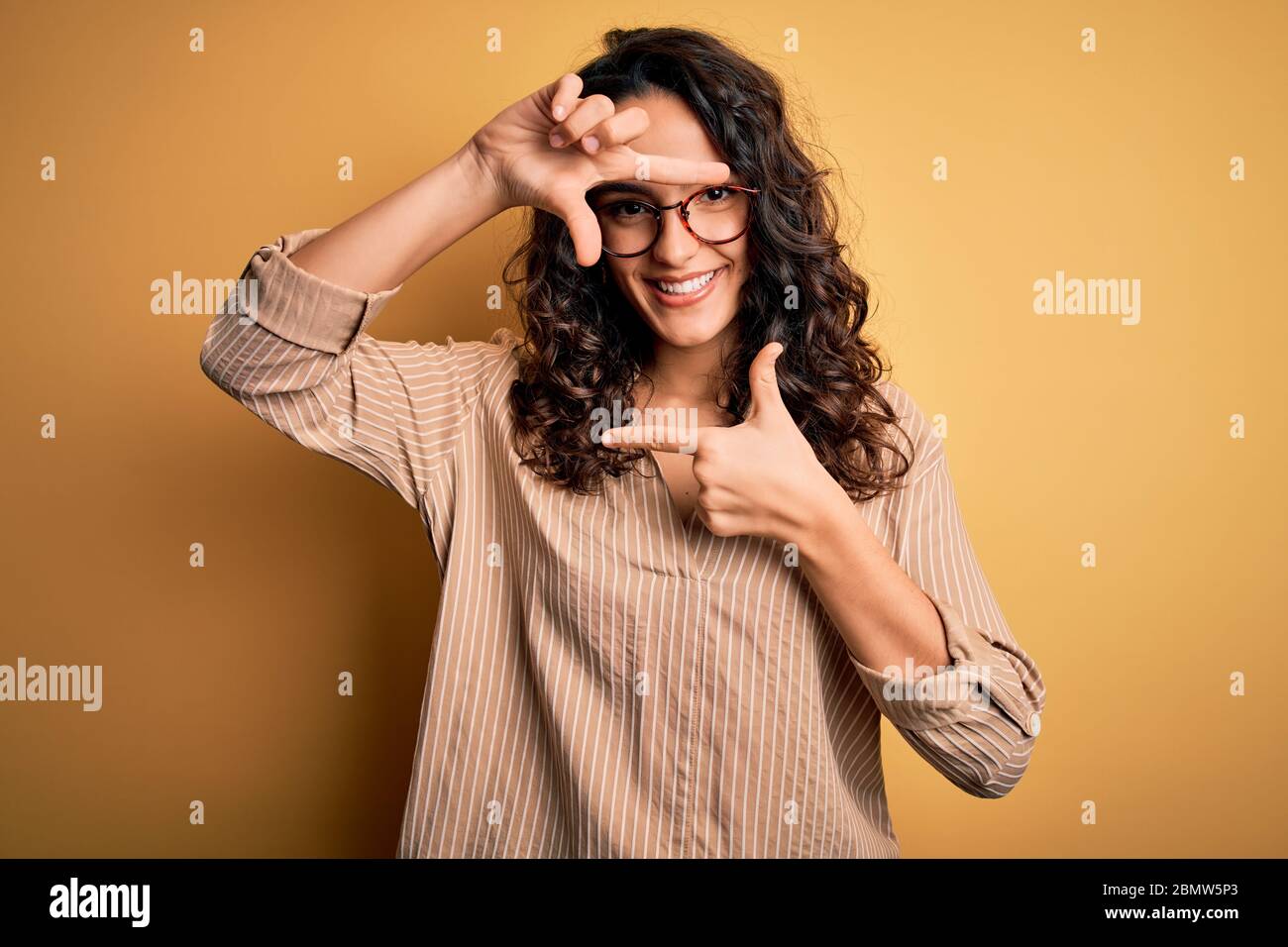 Beautiful woman with curly hair wearing striped shirt and glasses over ...