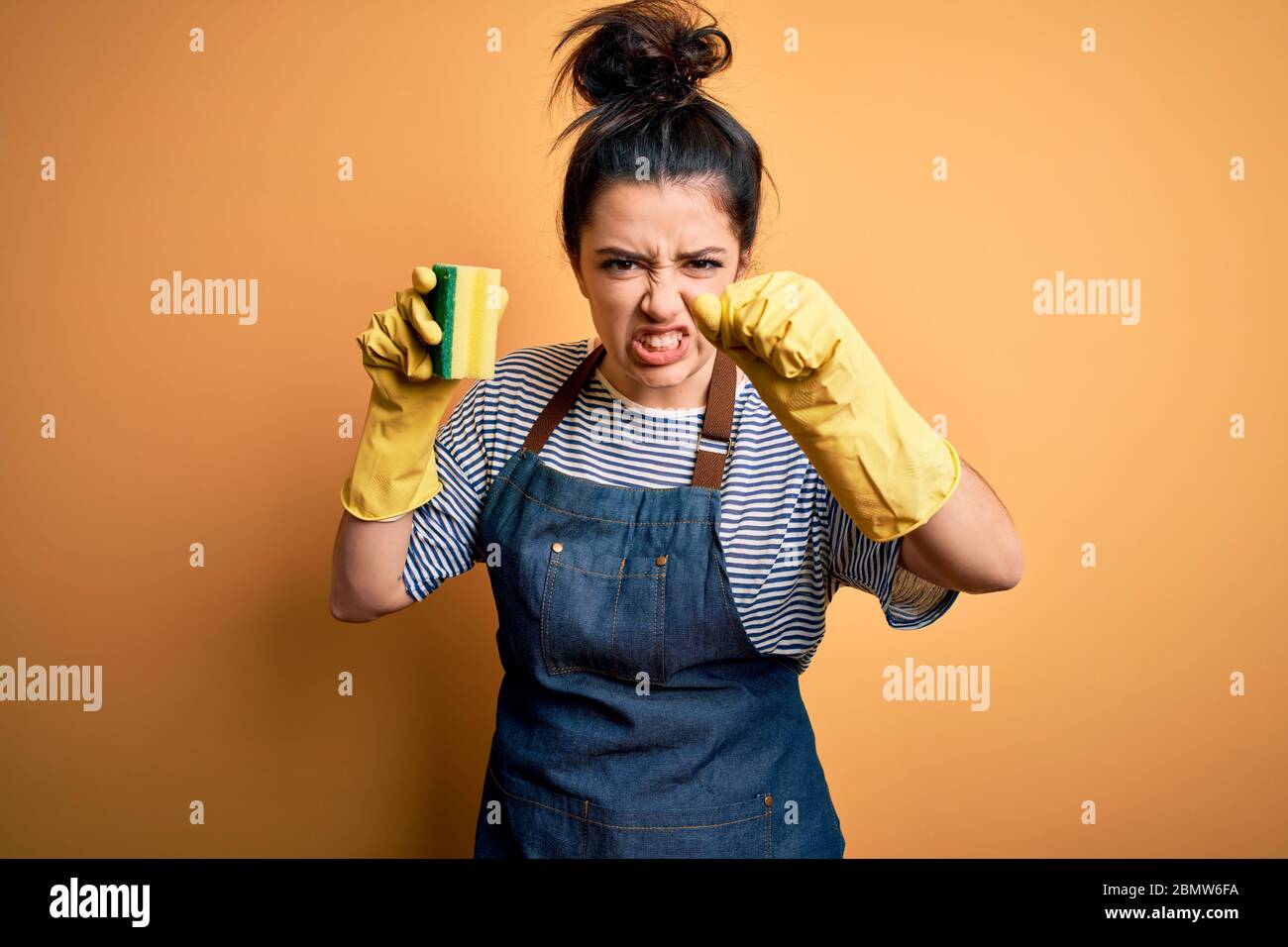 Young brunette cleaner woman wearing housekeeping gloves holding ...