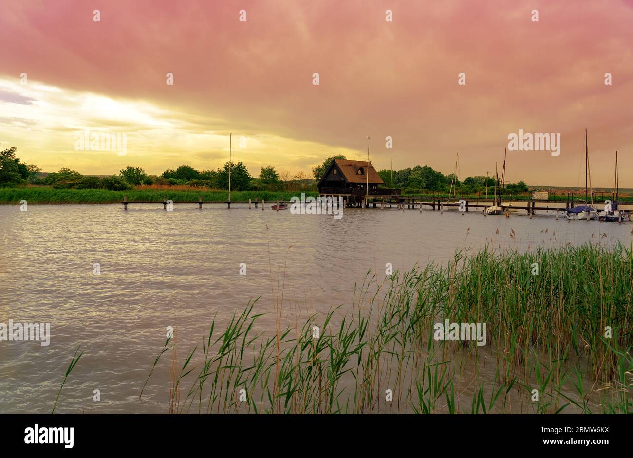 peaceful nature at the Lake Fertő in Hungary with wooden pier bungalows cabins on the lake and straw in the water at sunset Stock Photo