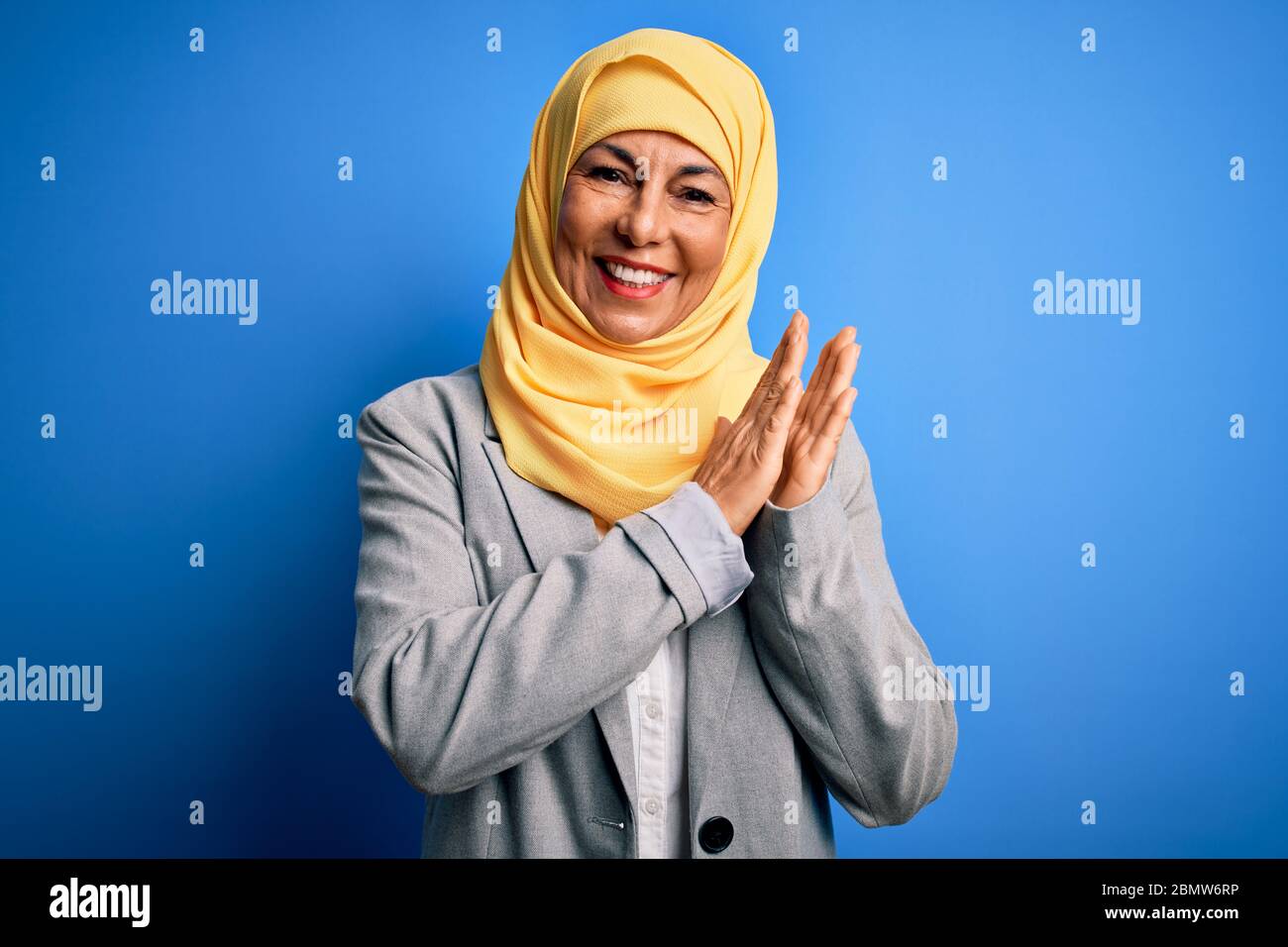 Middle age brunette business woman wearing muslim traditional hijab over blue background clapping and applauding happy and joyful, smiling proud hands Stock Photo