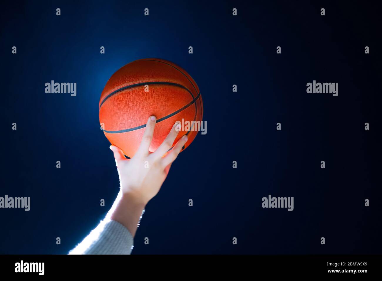 Close up of professional basketball player holding a ball in the hand. Street basketball athlete with a ball and blue sky in the background Stock Photo