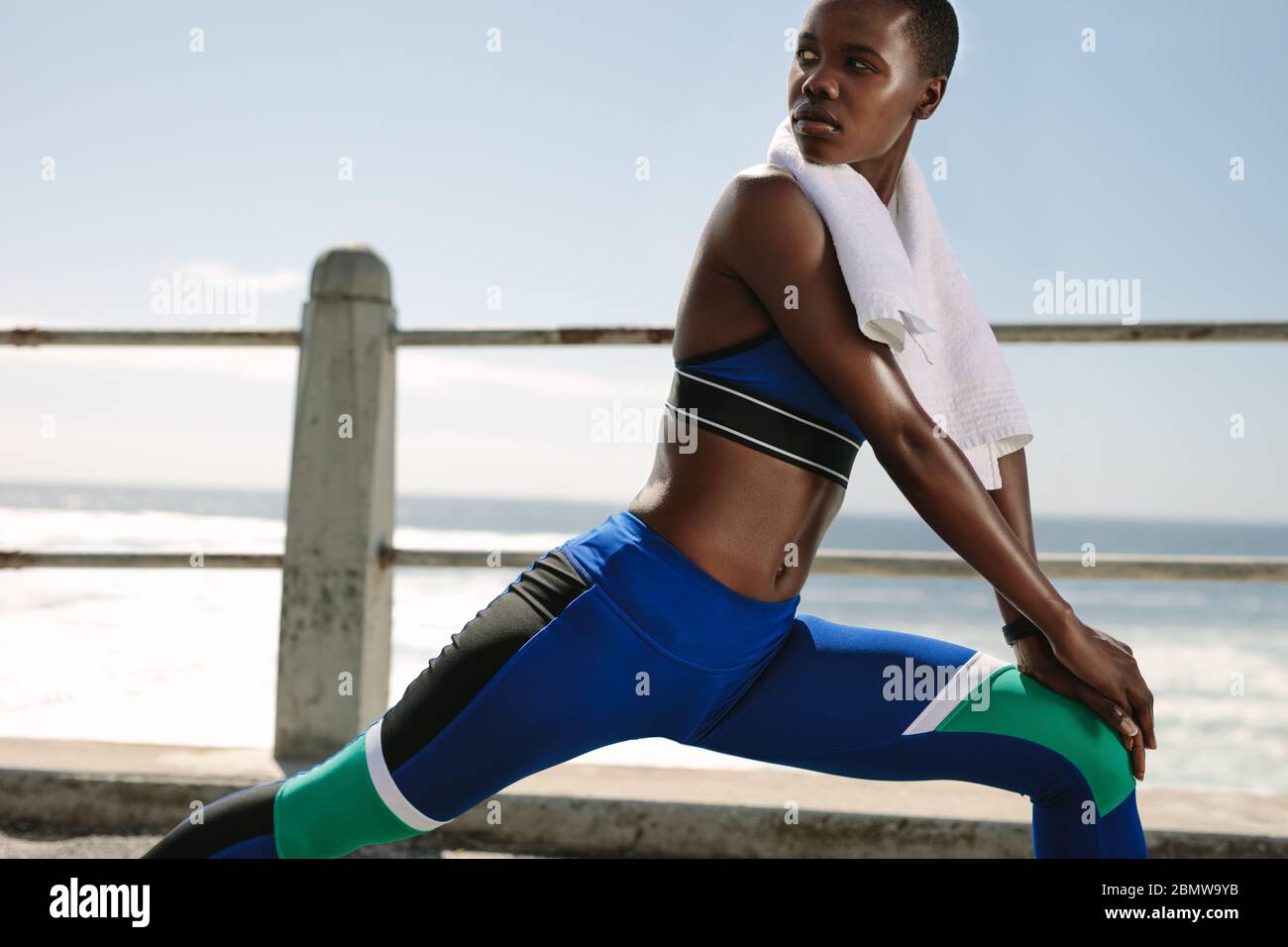 Woman runner exercising outdoors. Female runner in sportswear doing some stretching workout and looking away. Stock Photo