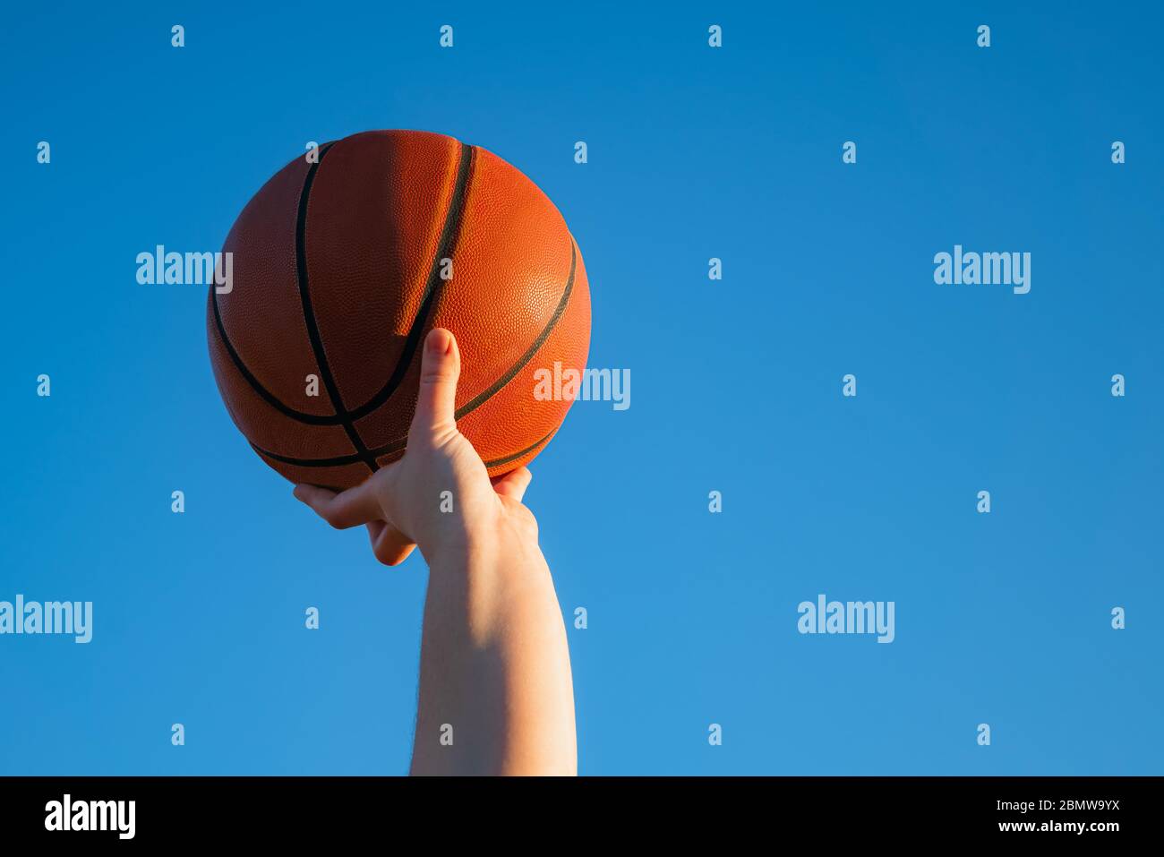 Close up of professional basketball player holding a ball in the hand. Street basketball athlete with a ball and blue sky in the background Stock Photo