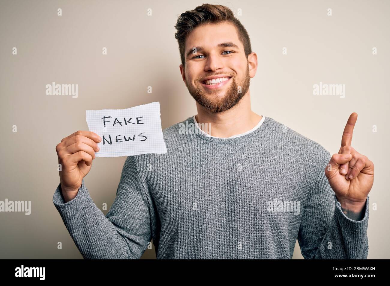 Young blond man with beard and blue eyes holding paper with fake news ...