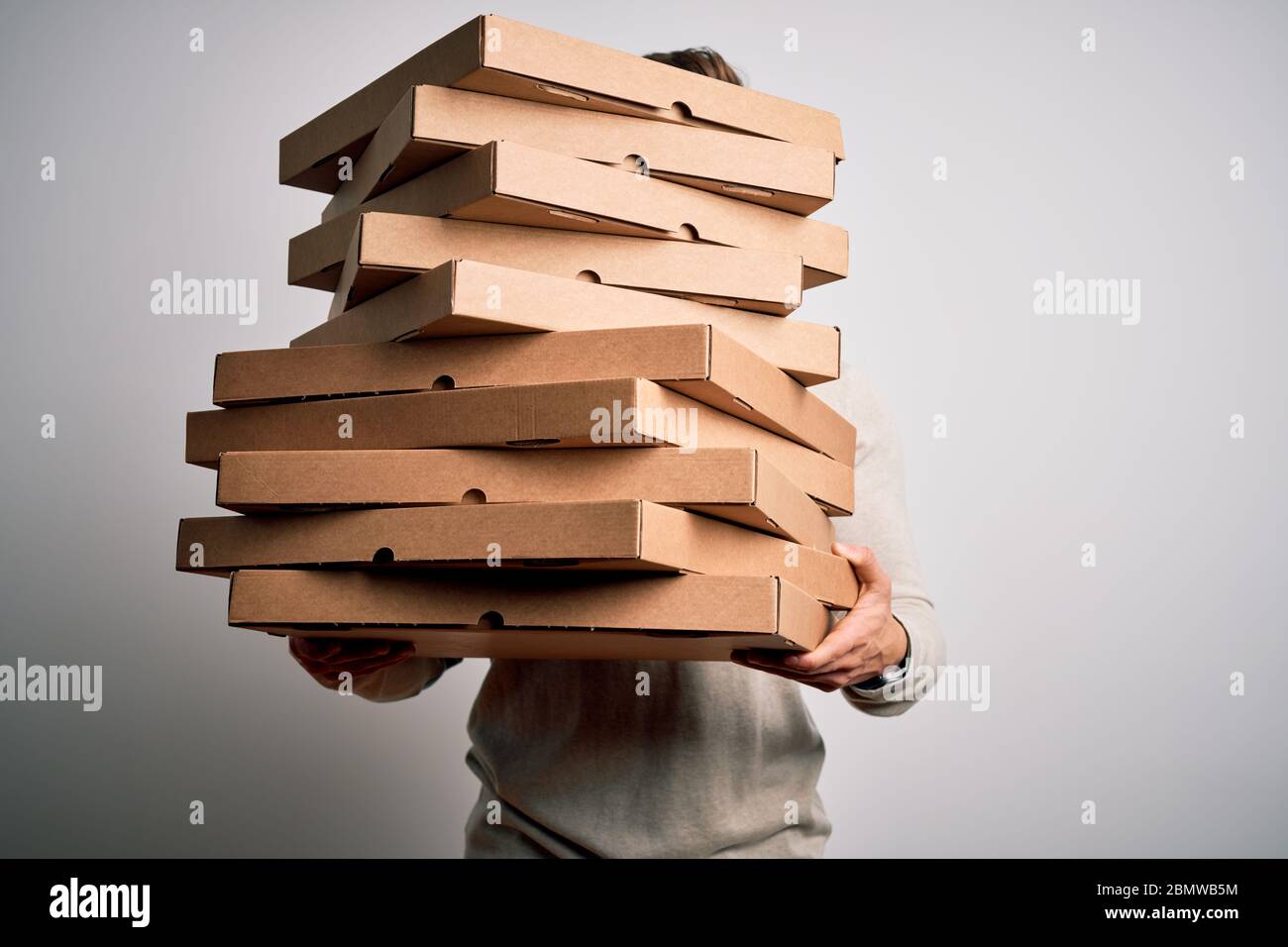 Deliveryman holding stack of caron boxes of italian pizza standing over isolated white background Stock Photo