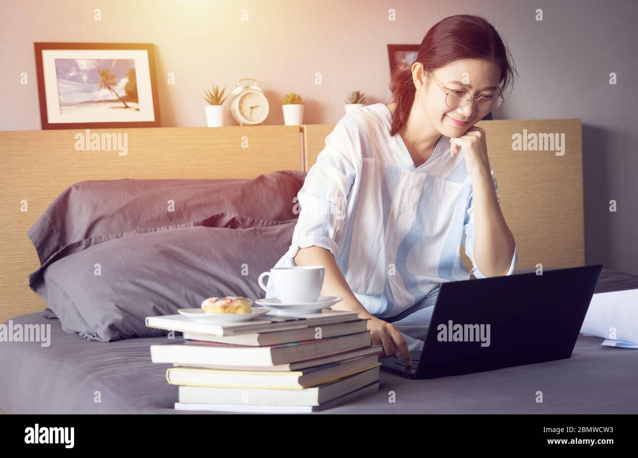 working from home, new normal concept. attractive happy woman working with laptop computer on bed from her room during self isolation. new normal Stock Photo