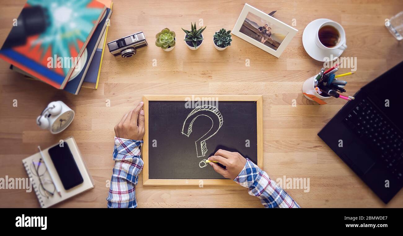 hand holding yellow chalk with a question mark on chalkboard on wooden office desk, top view. creative idea occupation concept Stock Photo