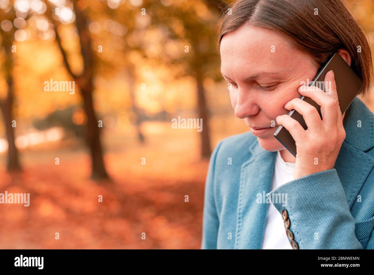 Businesswoman talking on mobile phone in autumn park, portrait of adult caucasian business person during telephone conversation Stock Photo