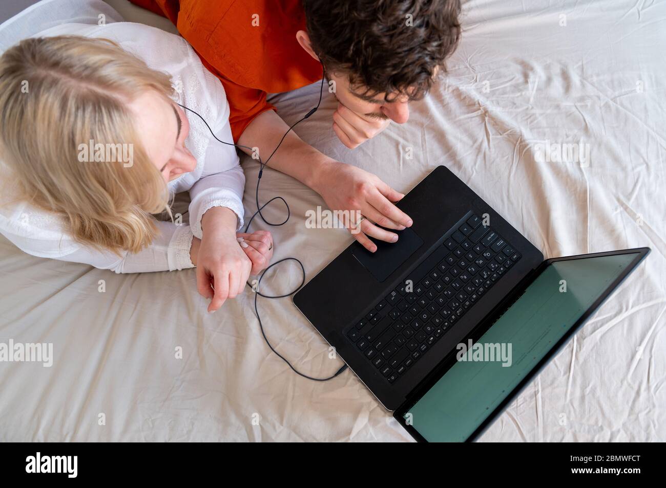 Smiling young adult couple using laptop and headphones together top view Stock Photo