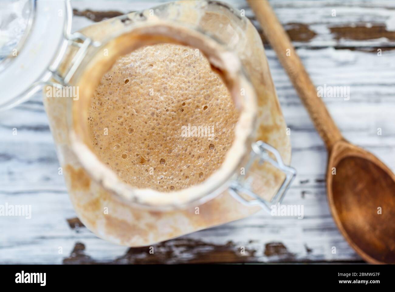 Abstract of active live whole wheat sourdough starter with a wooden spoon over a white rustic wood table / background with free space for text. Stock Photo