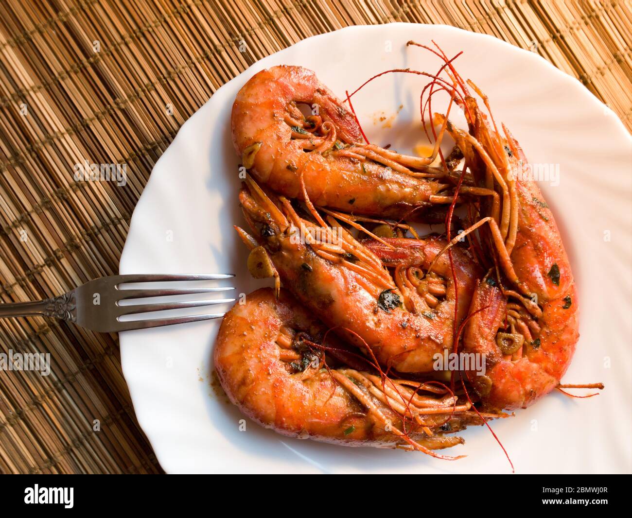 A fried lobster on a white plate, a straw lining under plate, fork, garlic, close up Stock Photo