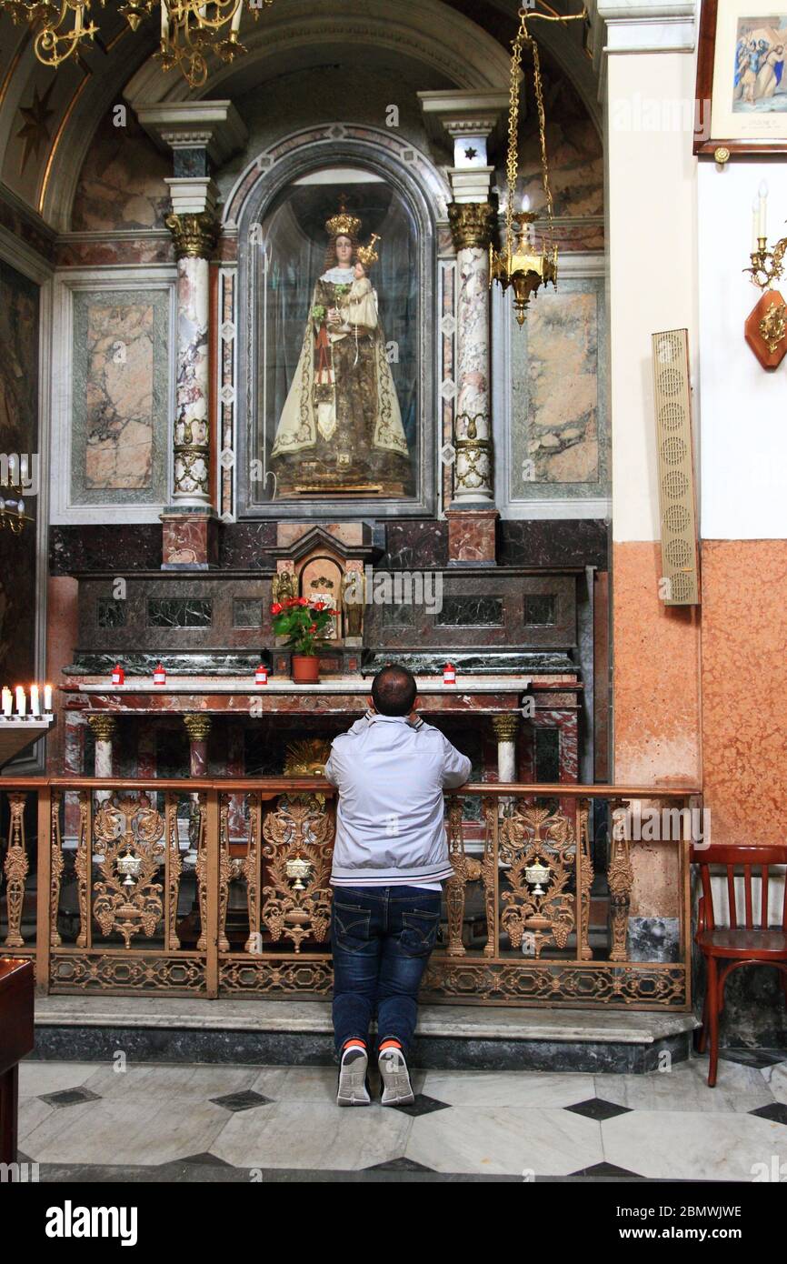 A young man is praying on his knees before the statue of Our Lady of Carmel after the reopening of the Shrine to personal prayer,. Stock Photo
