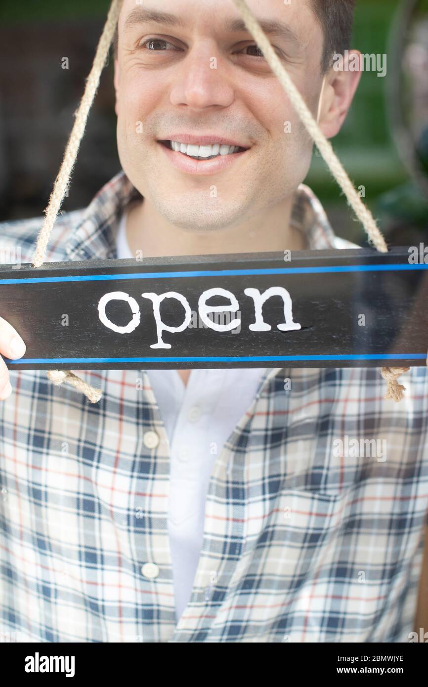 Close Up Of Smiling Male Small Business Owner Turning Around Open Sign On Shop Or Store Window Or Door Stock Photo