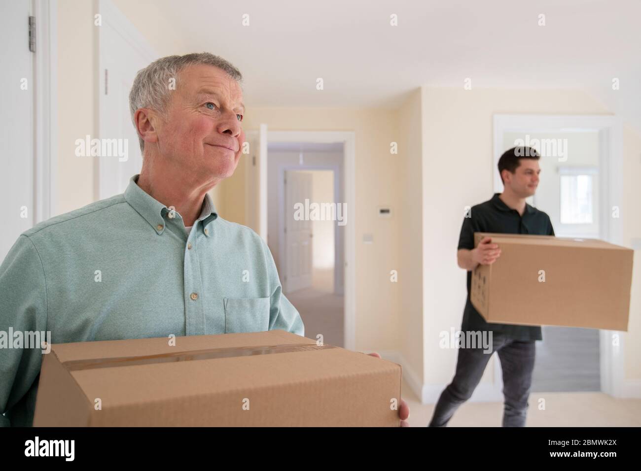 Senior Man Downsizing In Retirement Carrying Boxes Into New Home On Moving Day With Removal Man Helping Stock Photo
