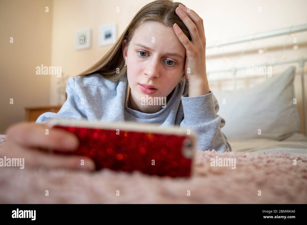 Worried Teenage Girl Lying On Bed With Mobile Phone Being Bullied Online Stock Photo