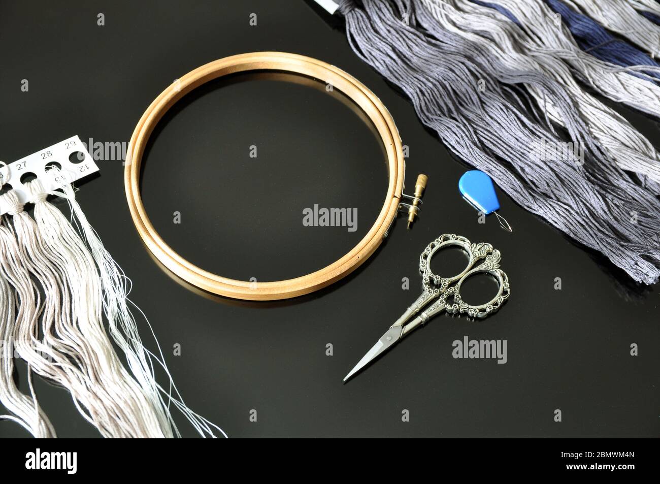 Accessories for needlework. Hoop, multi-colored threads, scissors, needle-threader on a black background. Copy space. Stock Photo