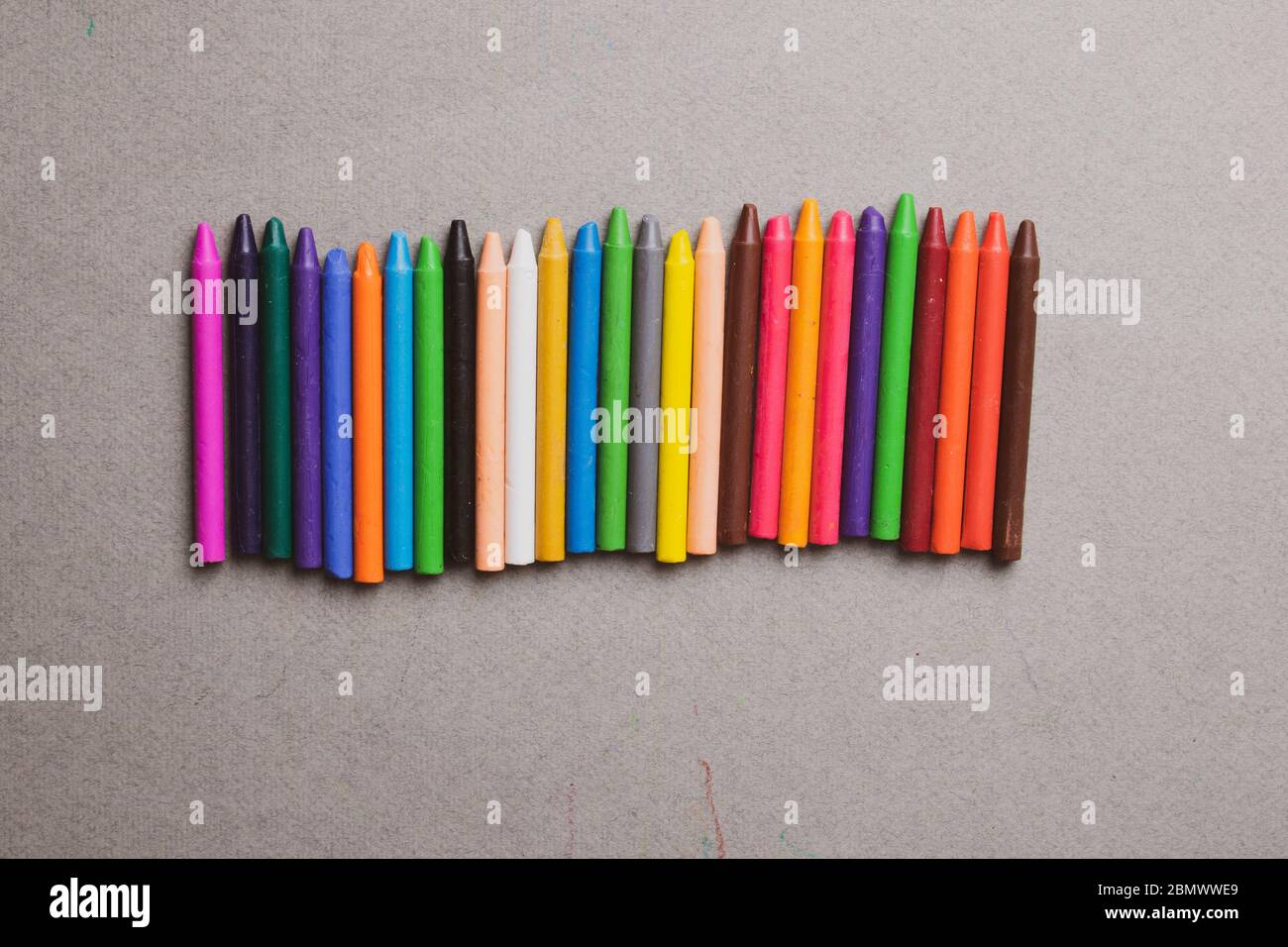 many multi-colored wax crayons on grey paper. Flat lay Stock Photo
