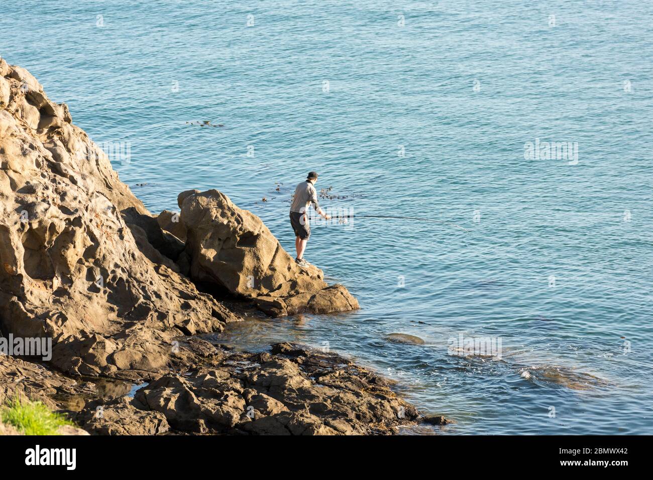 A man sea fishing off roacks in the South Pacific Ocean near Katiki Point New Zealand Stock Photo