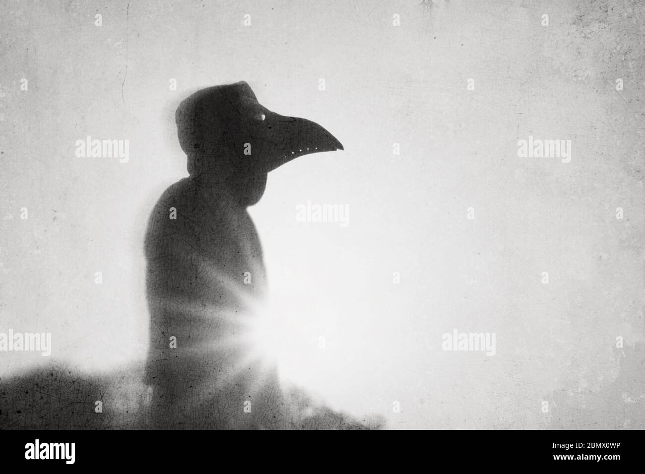 A scary hooded figure with a plague doctor mask, silhouetted against the sunset. With an abstract, experimental, grunge edit. Stock Photo