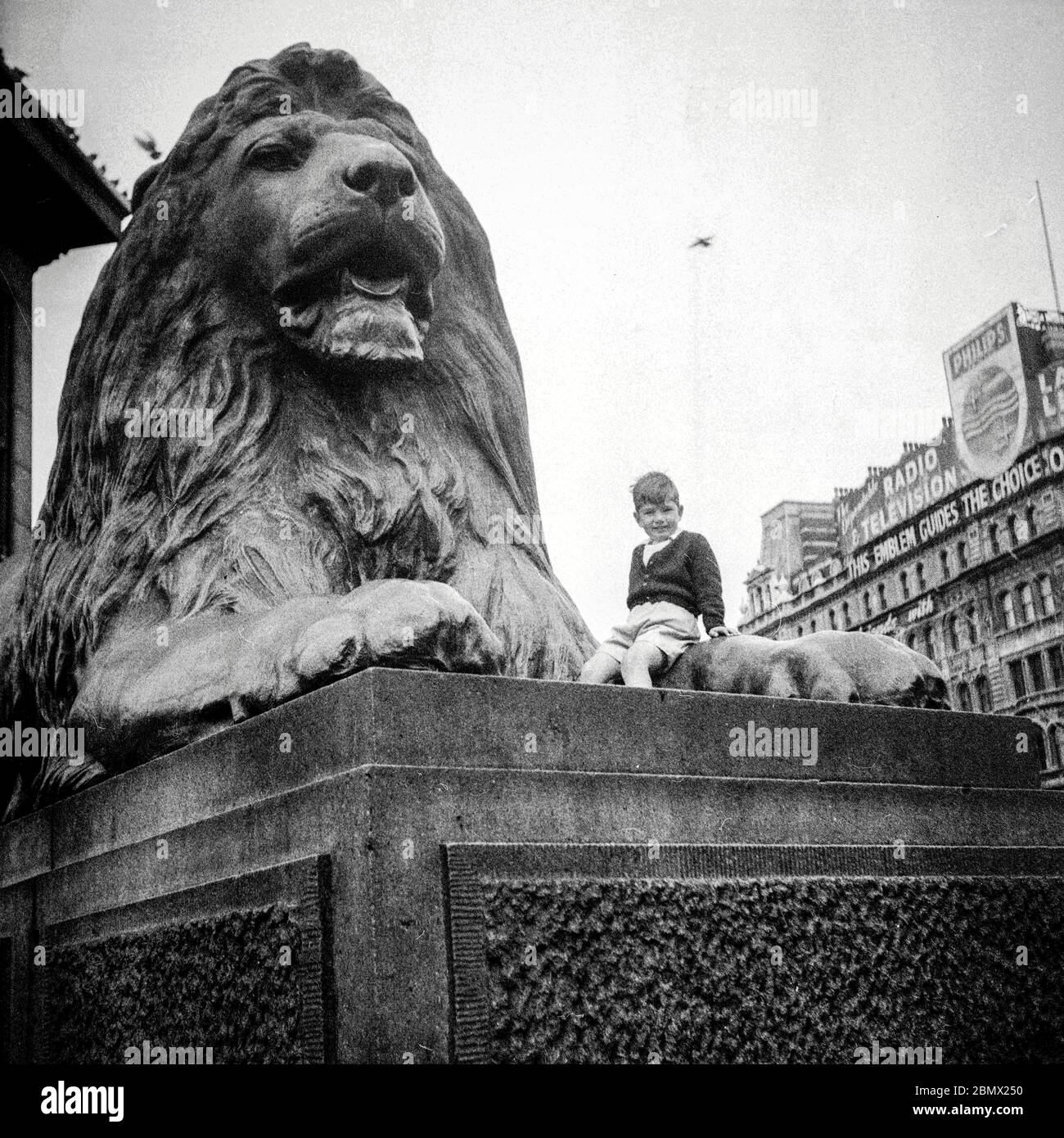 A boy sitting on a lion at Trafalgar Square, London 1955 Stock Photo