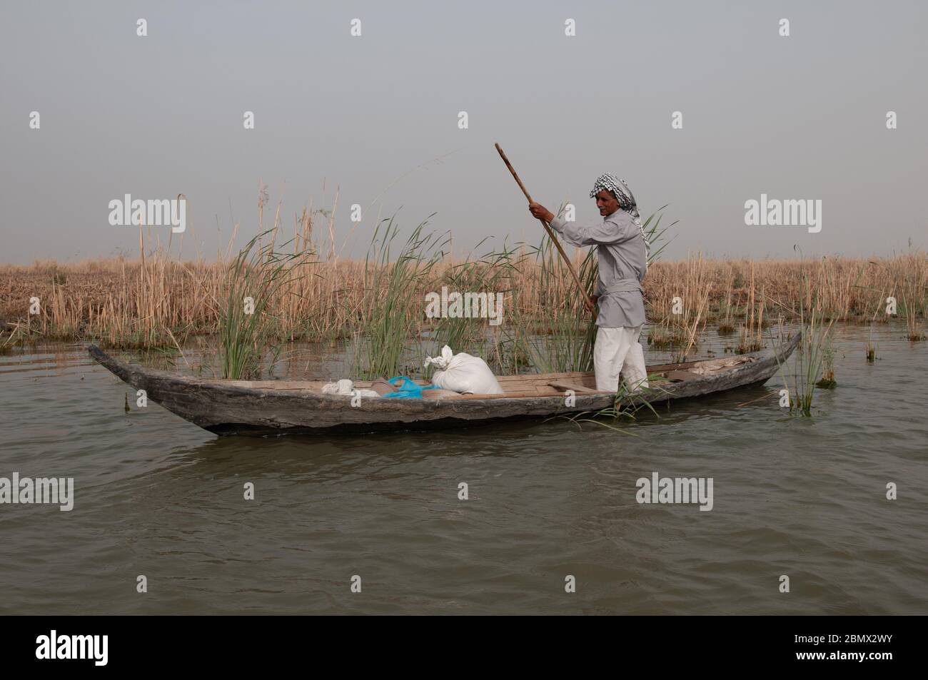A Marsh Arab boatman steers his mashoof (traditional boat) across a channel in the marshes of southern Iraq Stock Photo